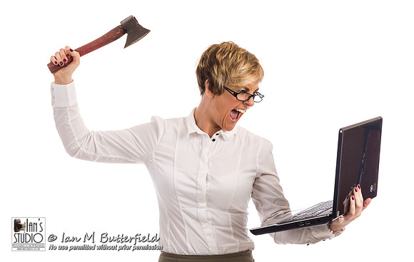 An angry business woman attacks a laptop with an axe